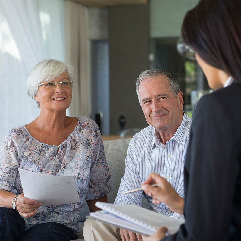 seniors-working-with-retirement-financial-planner senior couple listening to financial planner about their retirement while sitting on a couch